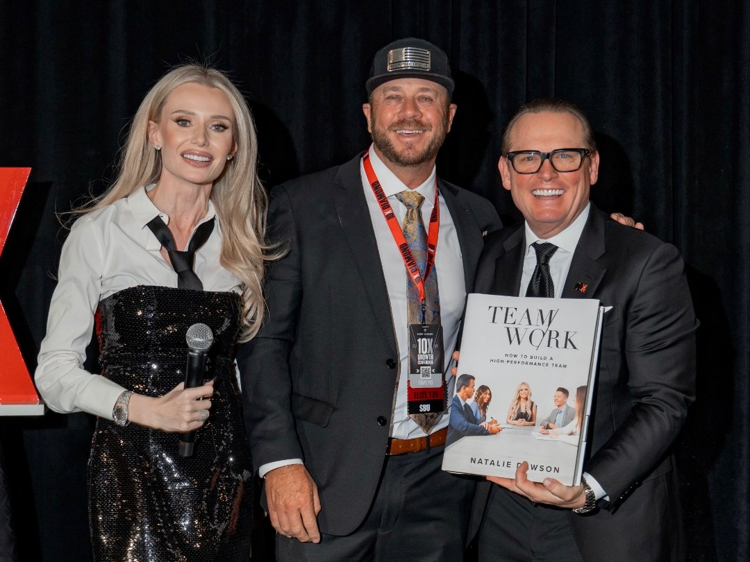 Jeremy Barker on the GrowthCon stage with Natalie Dawson, holding her book TEAMWORK at the Book Awards
